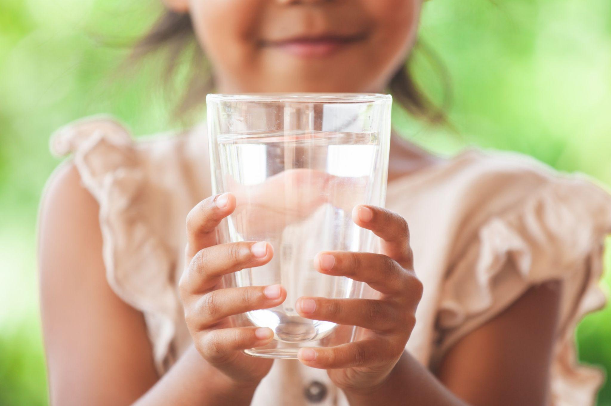 Happy child holds a clear glass of purified water outdoors
