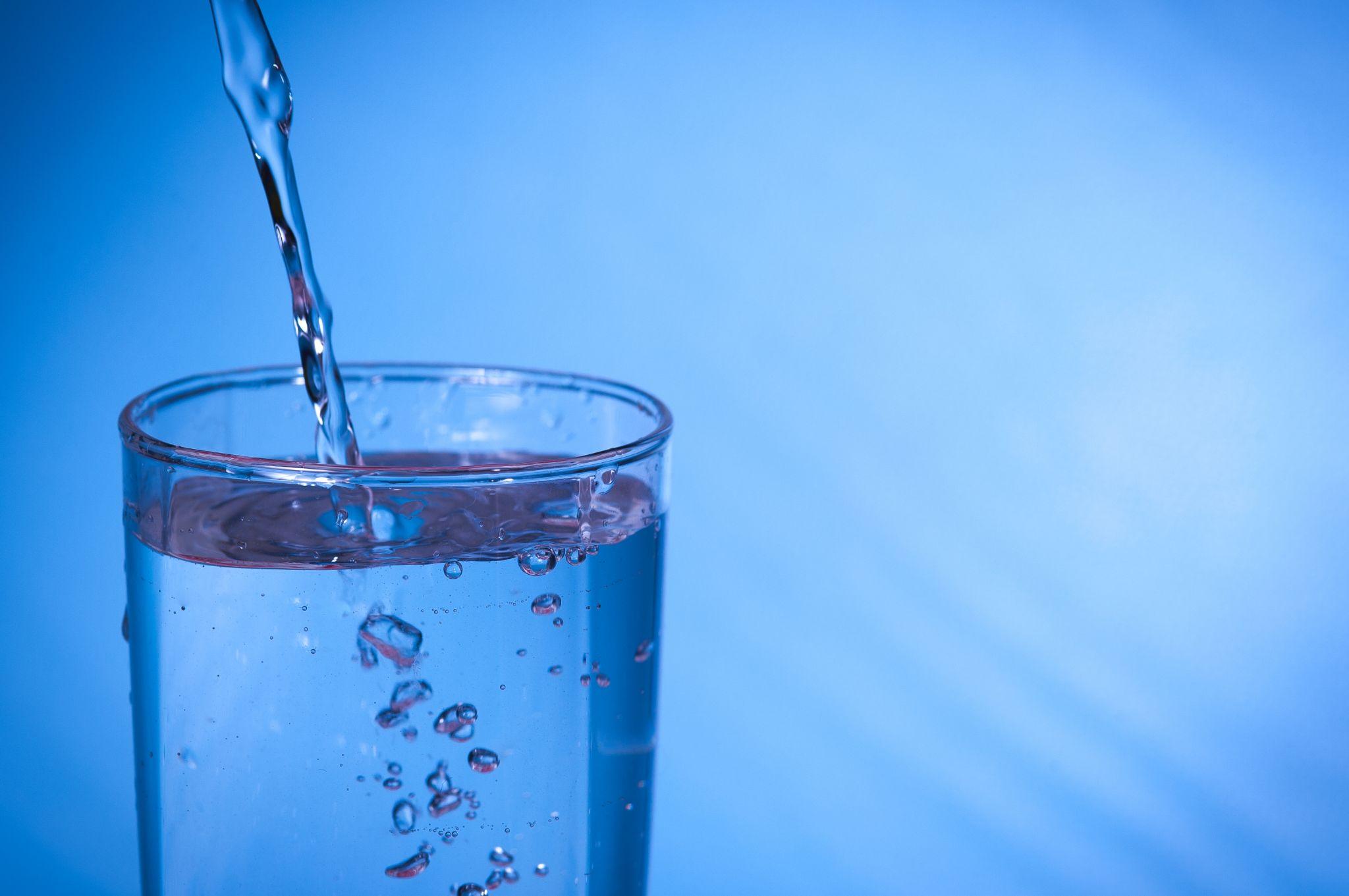 Clean purified water pouring into a glass against blue background