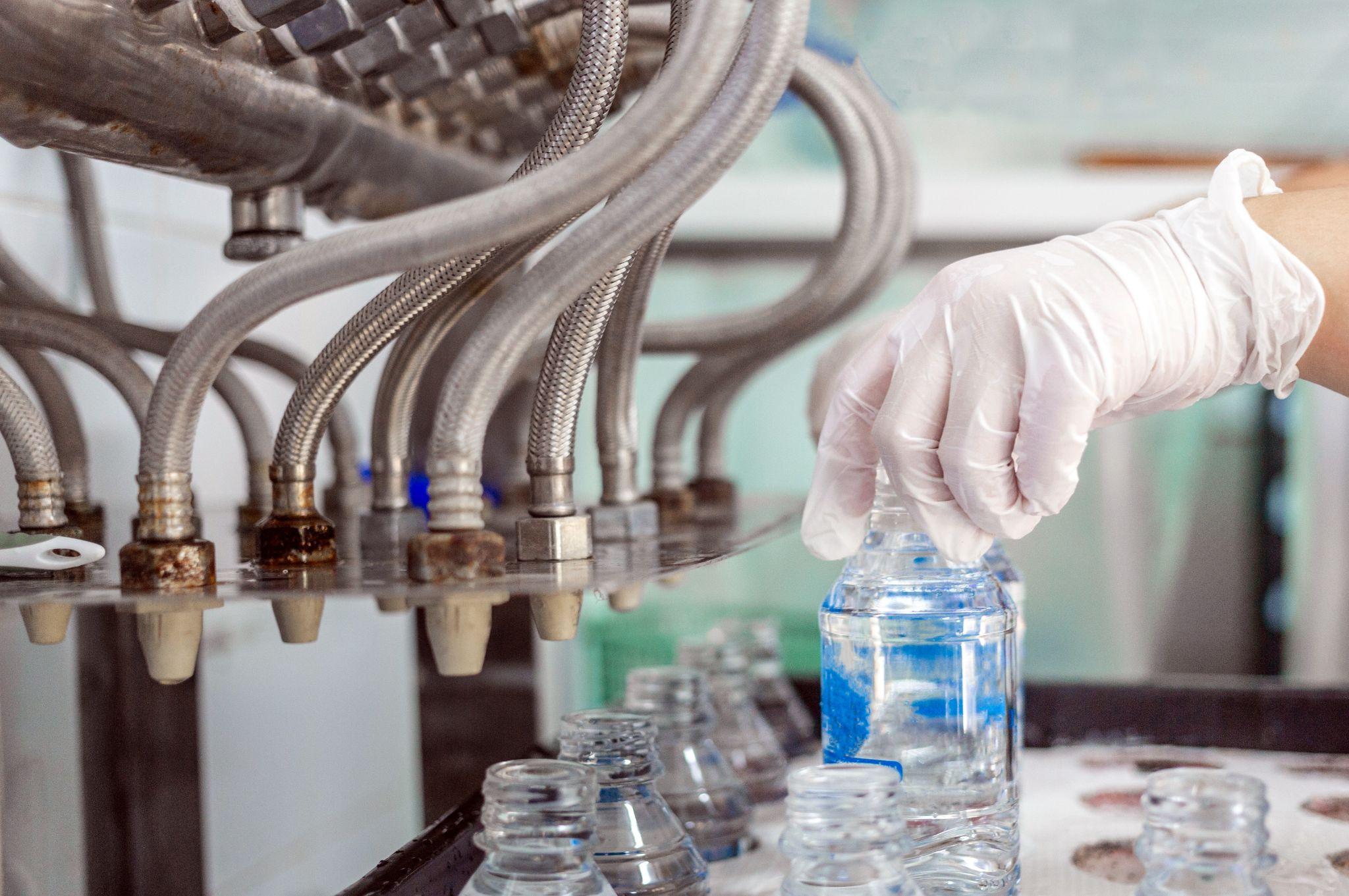 Hand with glove filling bottles during industrial purified water bottling process