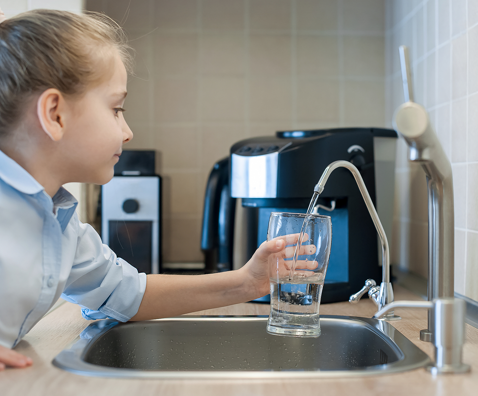Young girl filling a glass of fresh water from a reverse osmosis tap, enjoying fluoride-free drinking water.