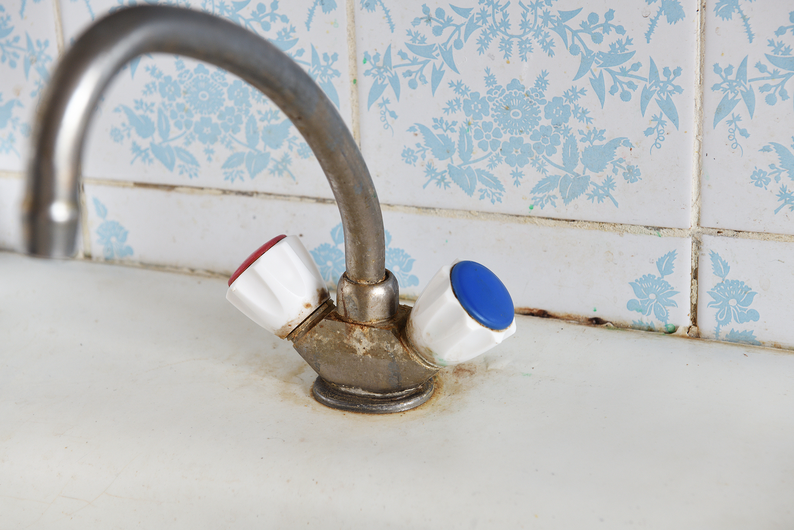 Old kitchen mixer tap showing rust and hard water stains on a white sink background