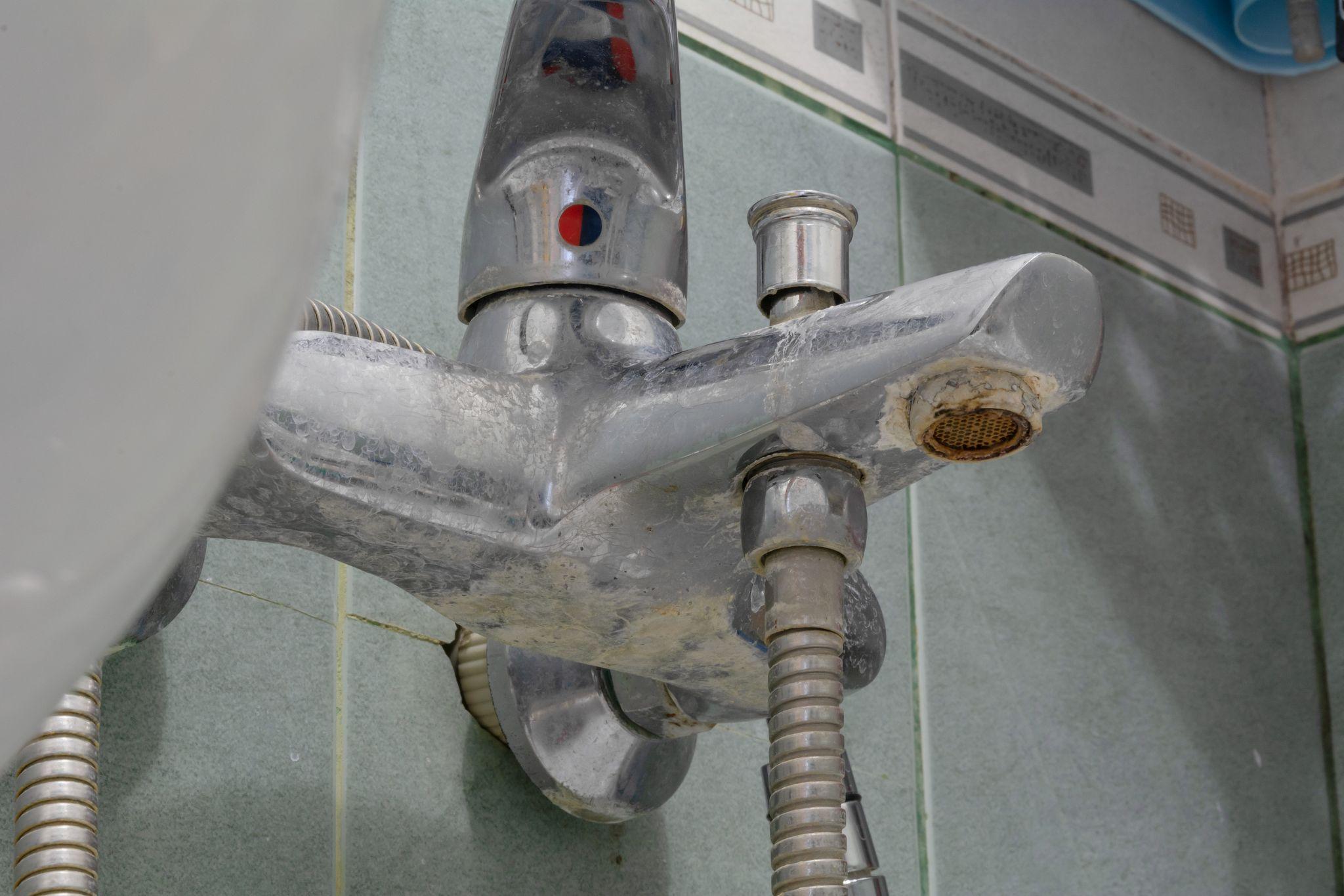 Close-up of a bathroom faucet with visible hard water stains and limescale buildup
