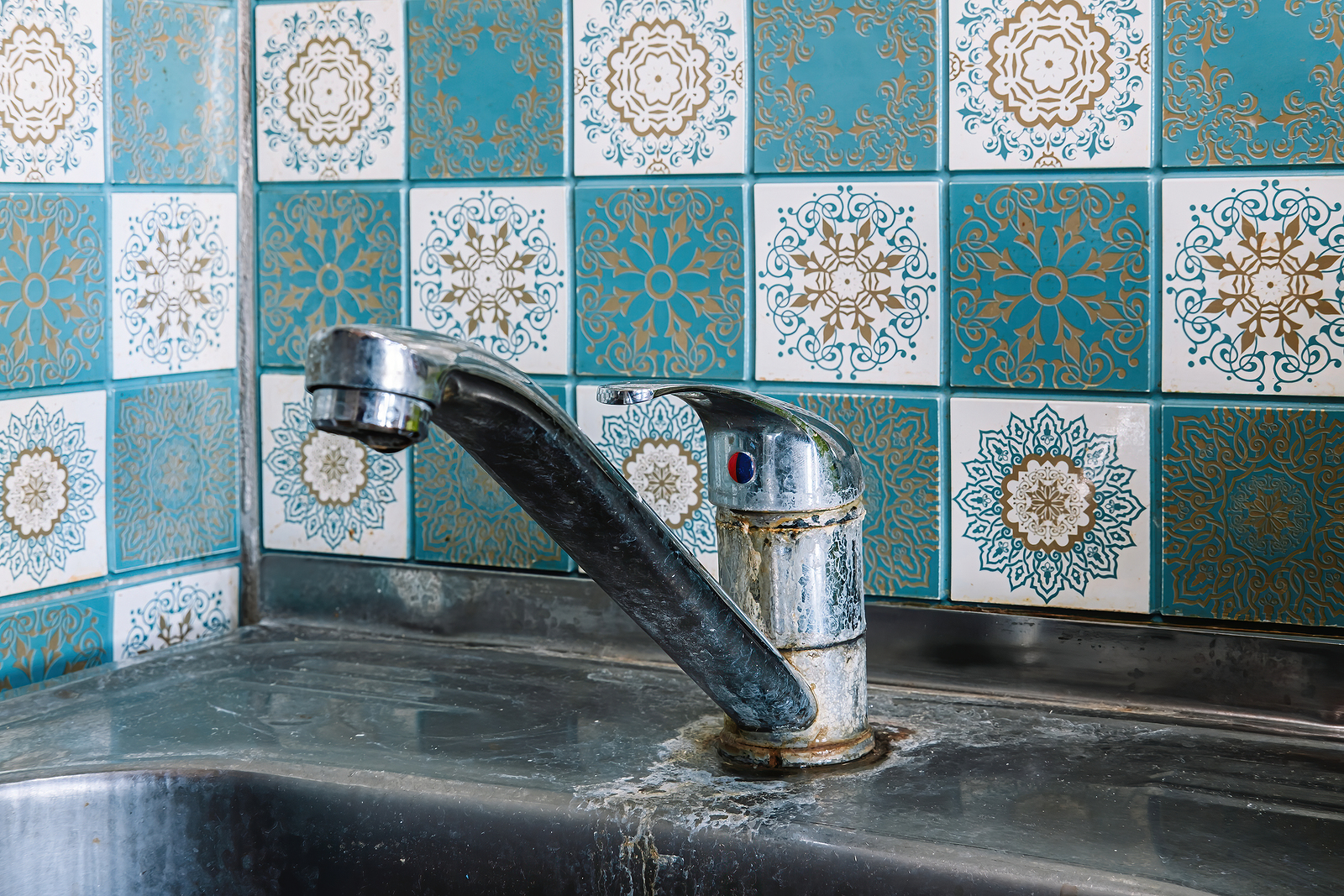 Stainless steel faucet and sink with significant hard water buildup and white mineral marks