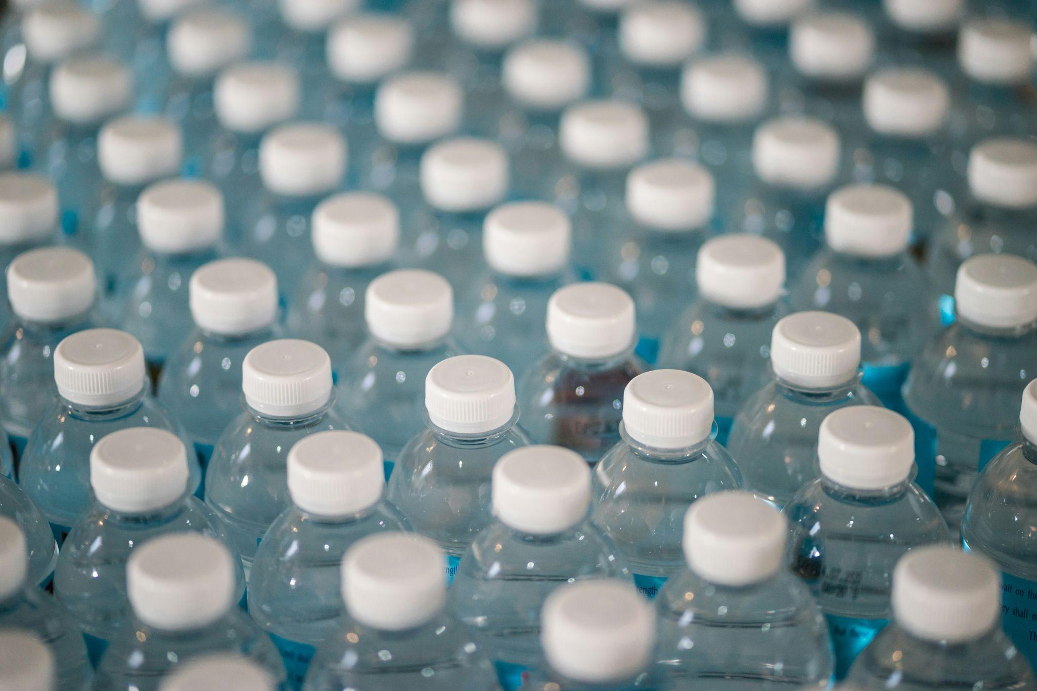 A large stockpile of plastic water bottles with white caps, highlighting concerns about chemical leaching and microplastics in bottled water.