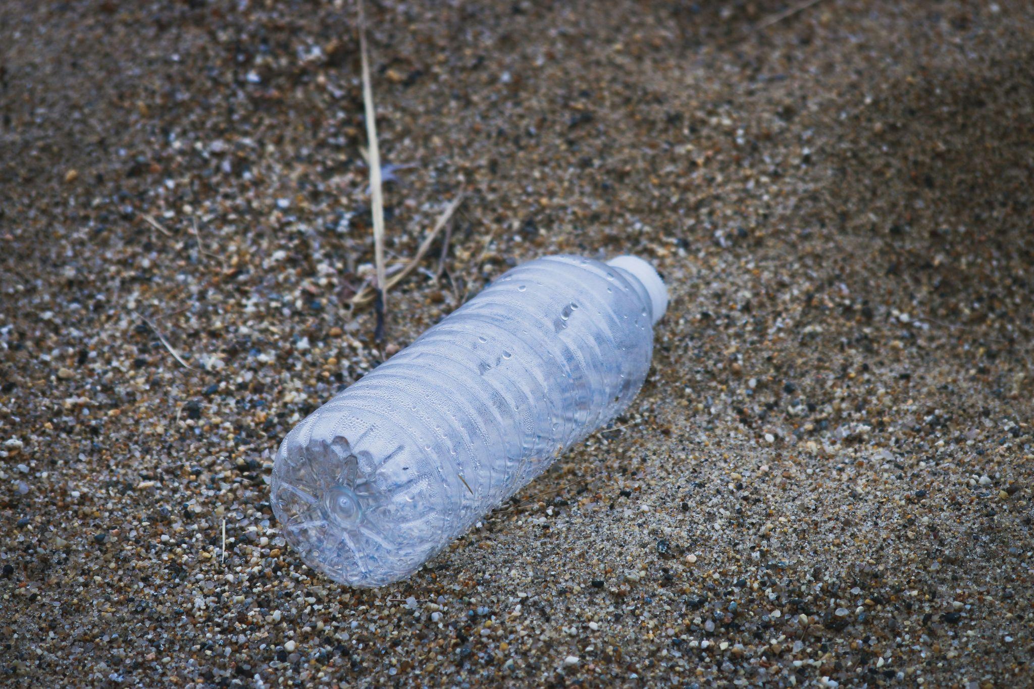 A plastic water bottle lying on sandy ground, emphasizing the litter problem and health risks from chemical leaching.