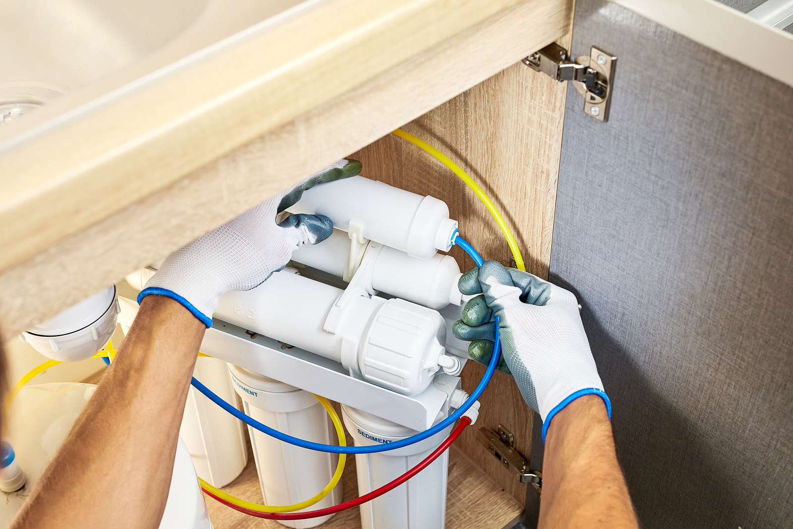 Technician installing an under-sink reverse osmosis filtration system to remove fluoride from household drinking water.
