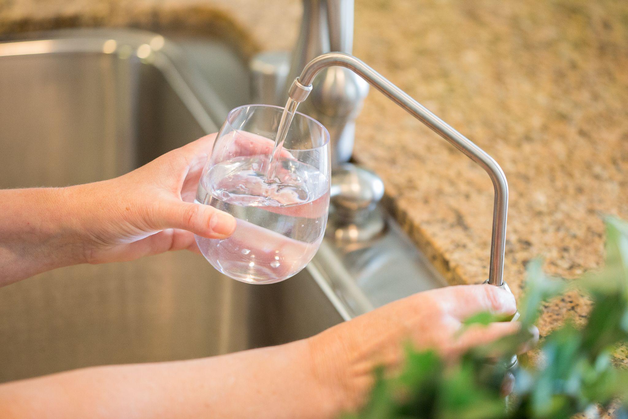 Clear filtered water being poured from a modern reverse osmosis faucet, showing the benefits of water filtration in San Diego homes