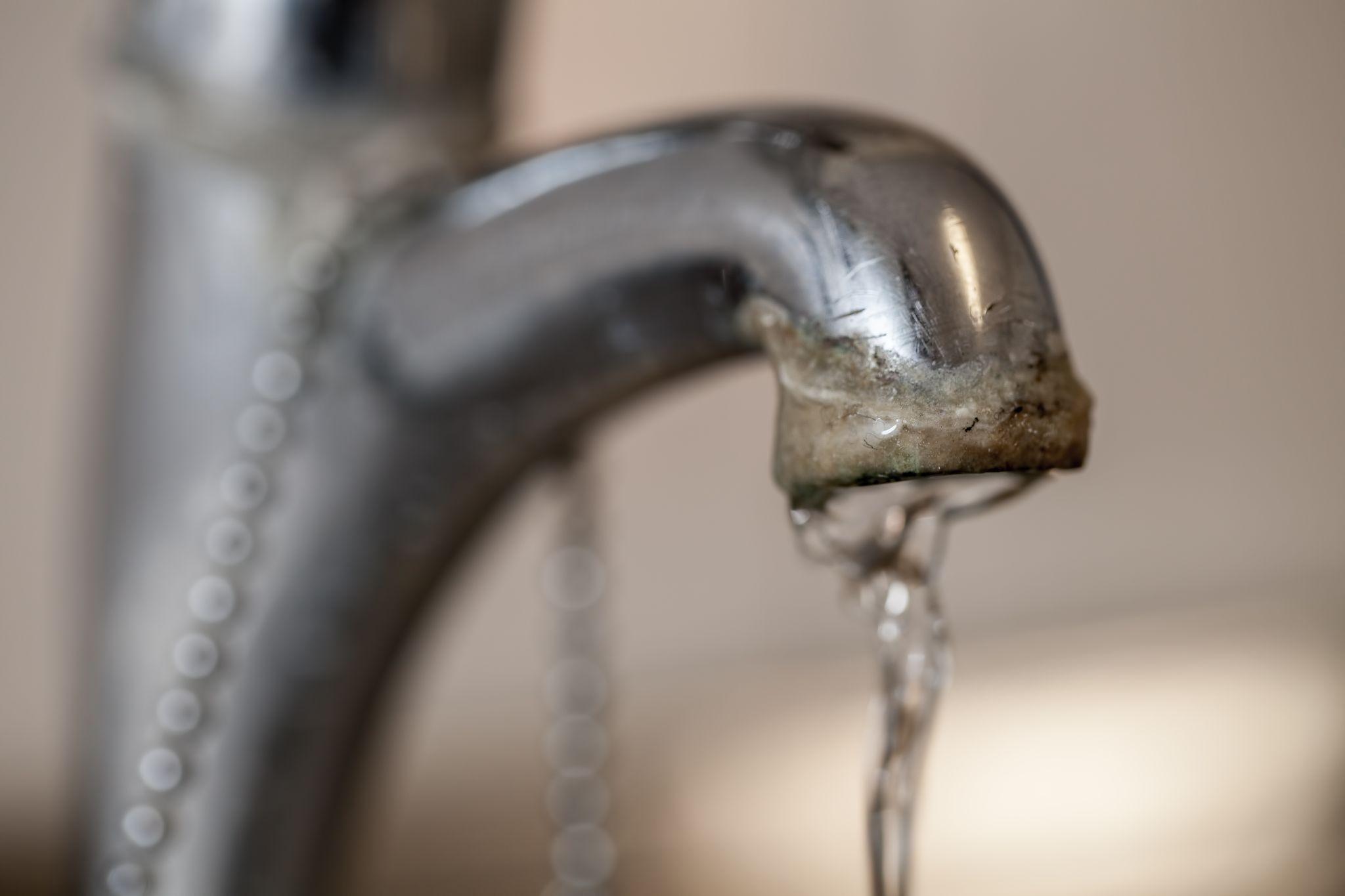 Water flowing from a faucet with visible scale and mineral deposits, illustrating the effects of hard water in Ventura