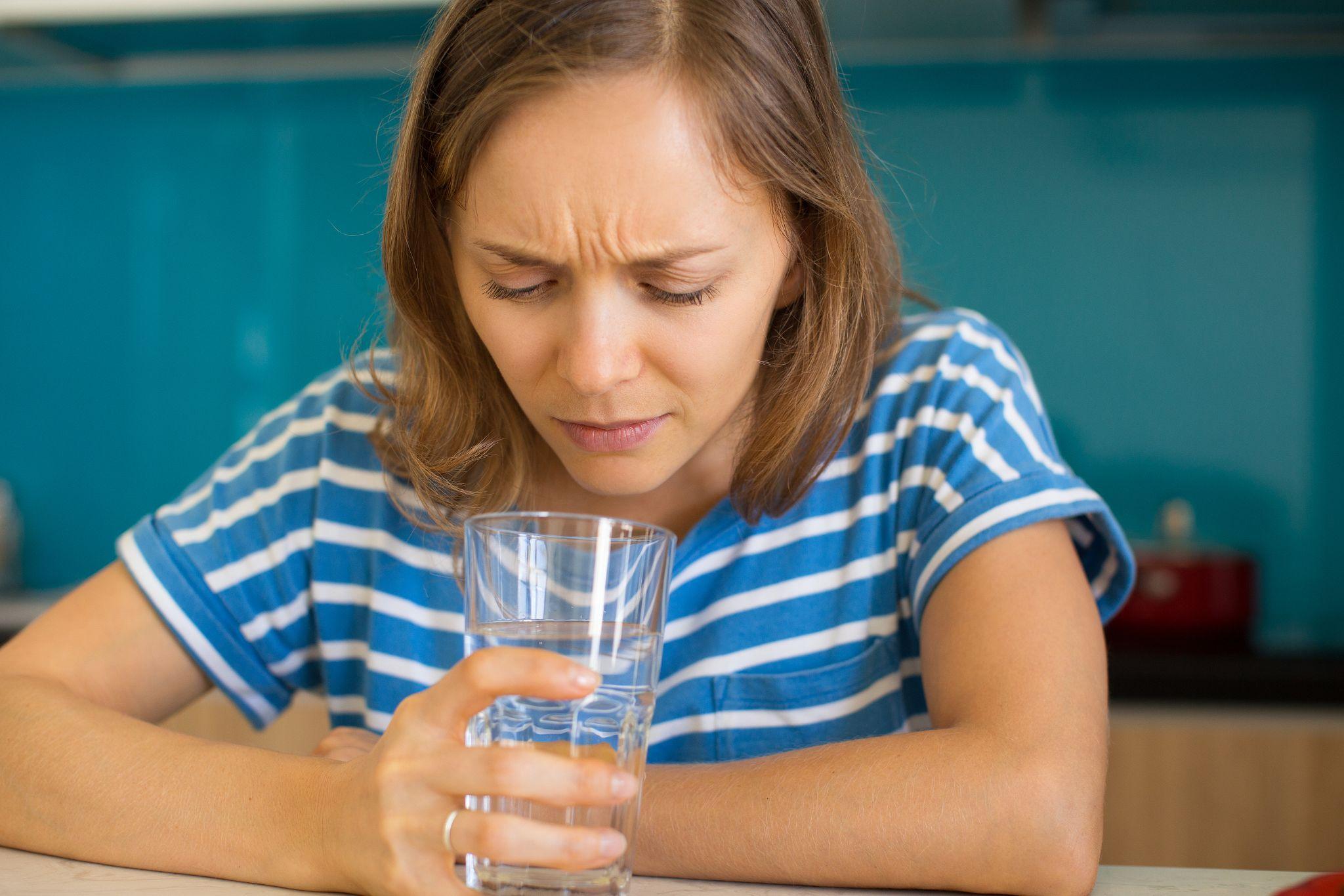 Woman looking worried while inspecting a glass of water at home, reflecting common doubts about San Diego tap water safety.